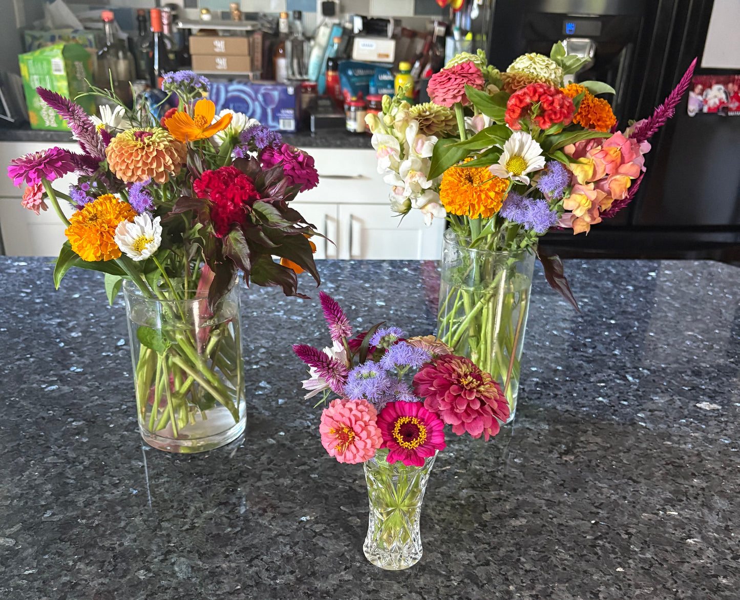 Colorful flowers in glass vases on a dark countertop with a store interior in the background.