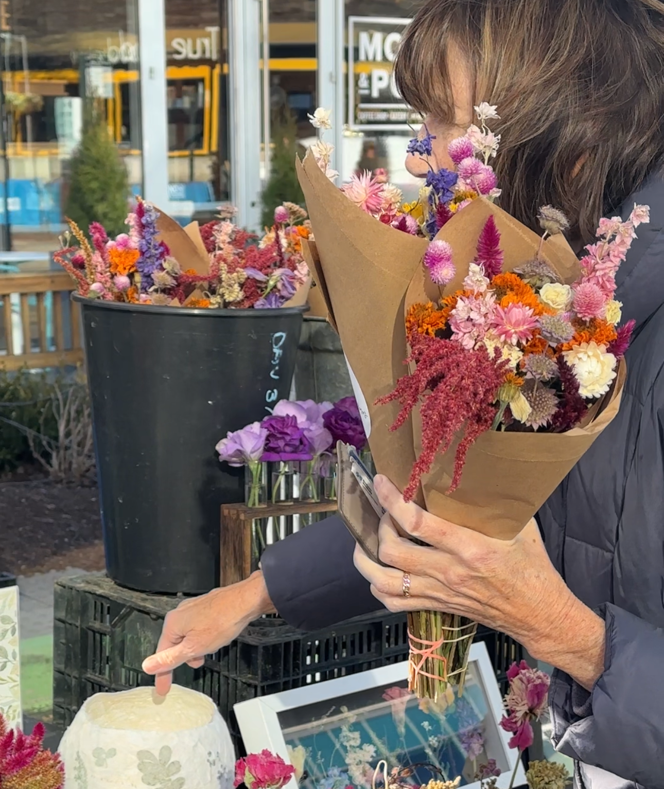 Person holding a bouquet of flowers in an indoor setting with various items on a table.